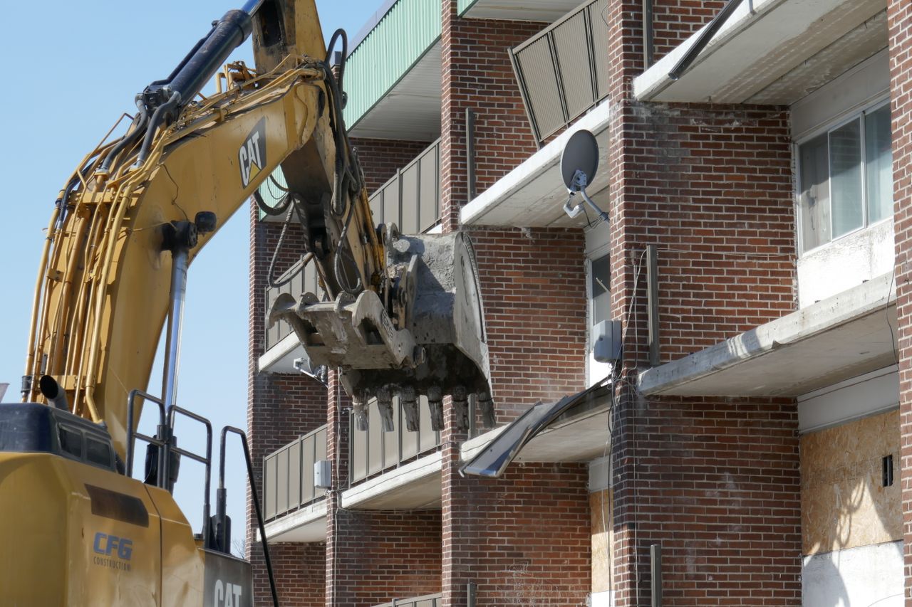 Excavator demolishing a brick residential building in an urban area.